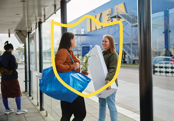 Twee vrouwen staan met IKEA aankopen voor de ingang van de winkel.