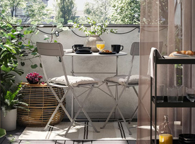 Klein balkon met grijze RUNNEN vlonders, SUNDSÖ tafel en stoelen en gezellige accessoires zoals lampjes, planten en kussens.
