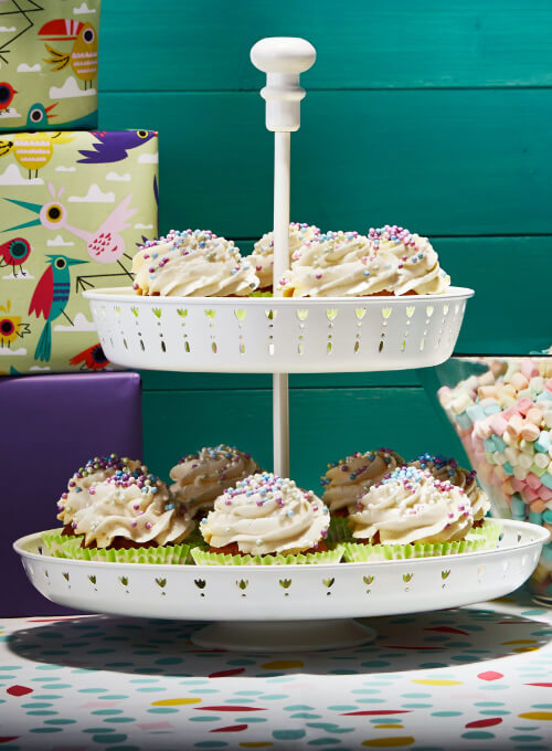Een wit taartplateau met twee verdiepingen waarop cupcakes met wit glazuur en hagelslag staan.