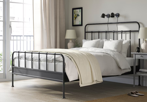Een zwart metalen bedframe staat opgemaakt in een beige slaapkamer