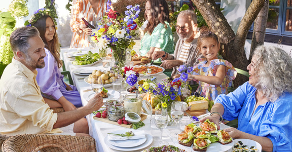 Mensen aan een lange buitentafel, gevuld met hapjes, drankjes en bloemen
