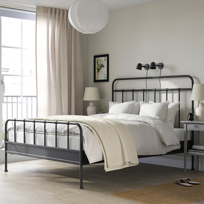 Een zwart metalen bedframe staat opgemaakt in een beige slaapkamer