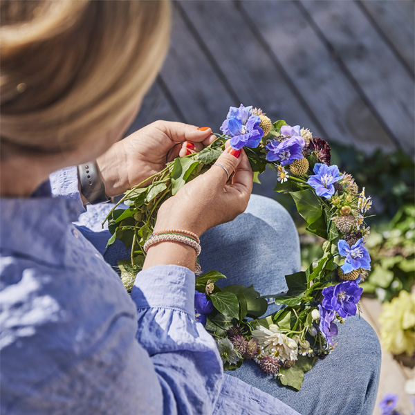 Vrouw maakt een krans met bladeren en paarse bloemen