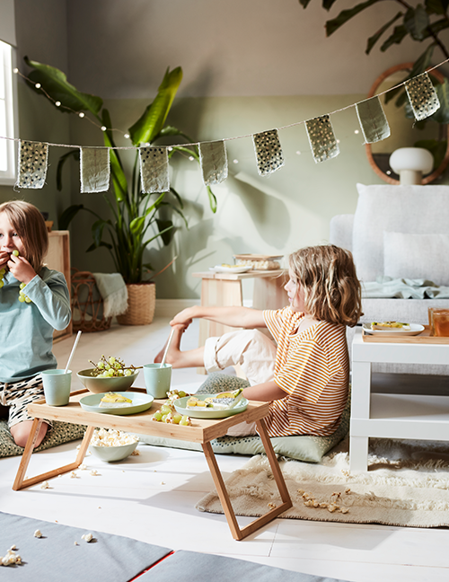 Twee kinderen zitten op de vloer van een Woonkamers naast een houten dienblad met borden eten.