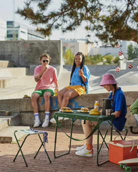3 jongeren zitten buiten met een groene klaptafelset, koelbox en eten