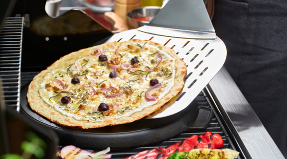 Pizza ligt op een pizzapan op de barbecue