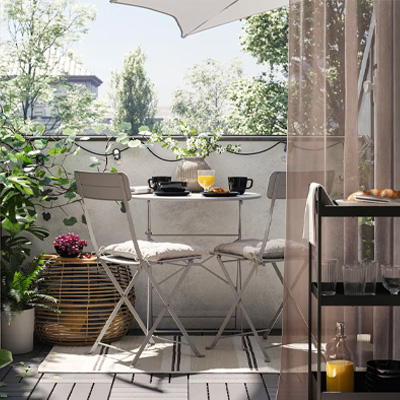 Klein balkon met grijze RUNNEN vlonders, SUNDSÖ tafel en stoelen en gezellige accessoires zoals lampjes, planten en kussens.